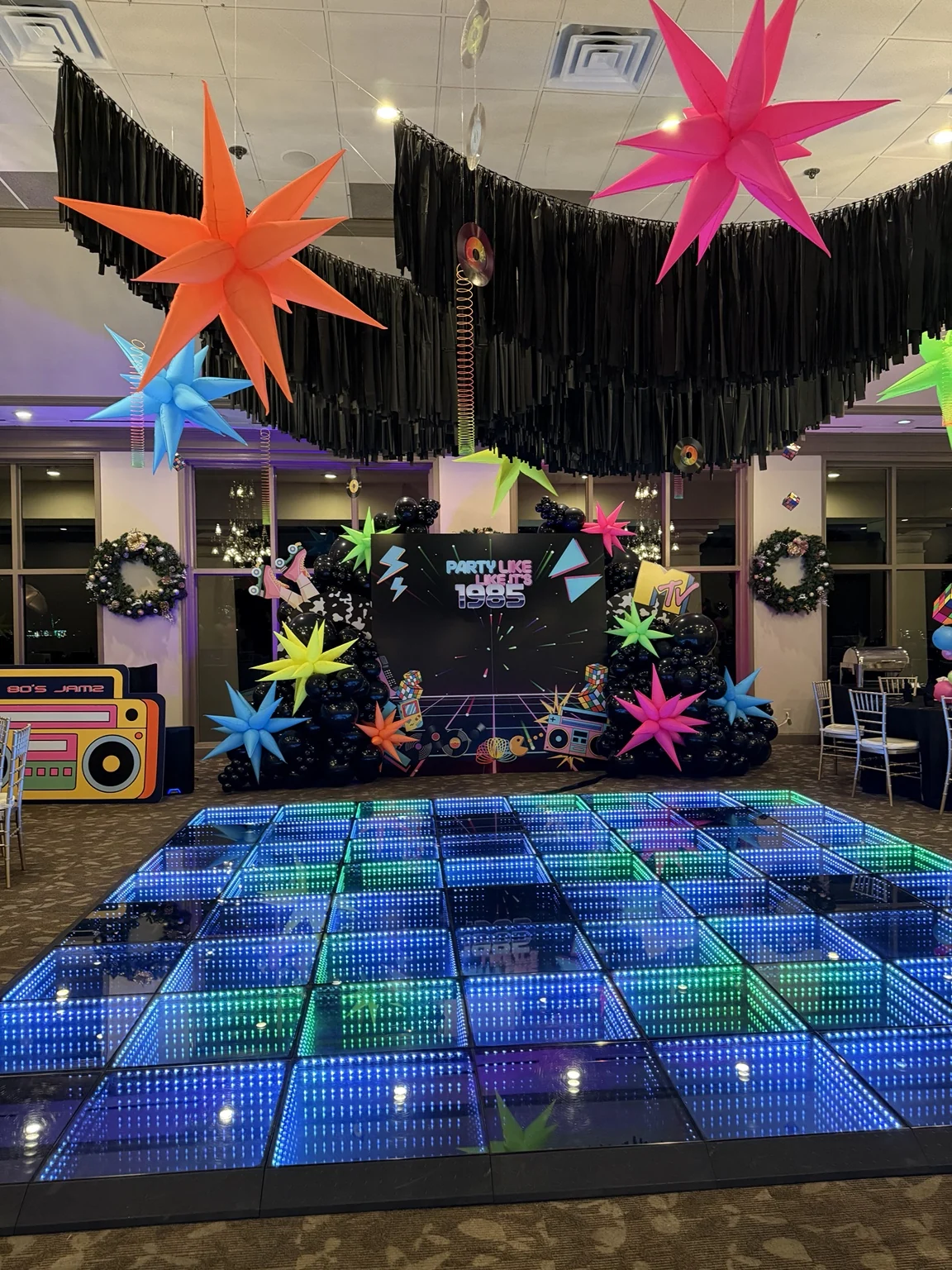 A completed 1980s party setup with a glowing dance floor, custom backdrop, and suspended decor