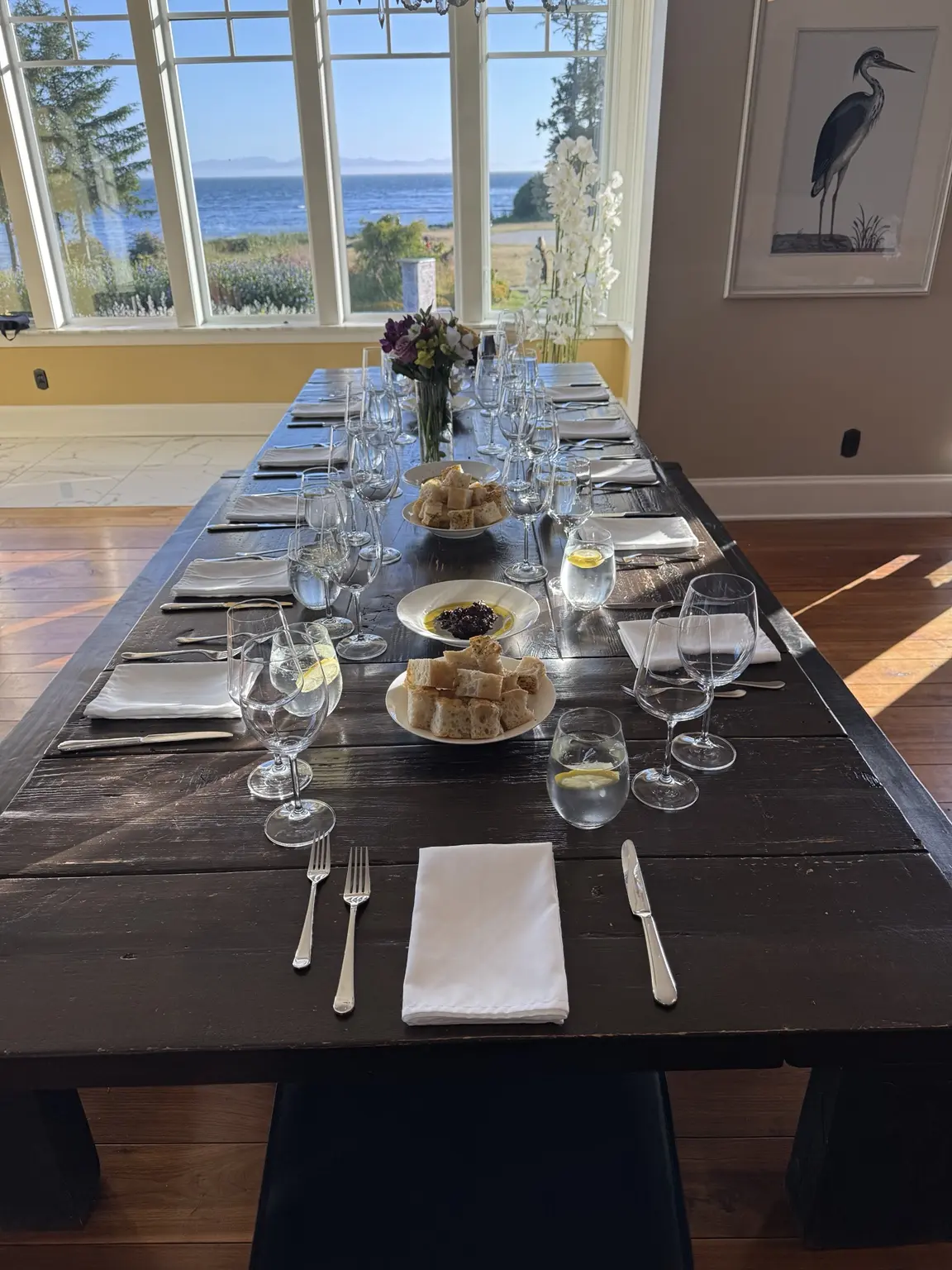 A long dinner table set beside windows overlooking the water